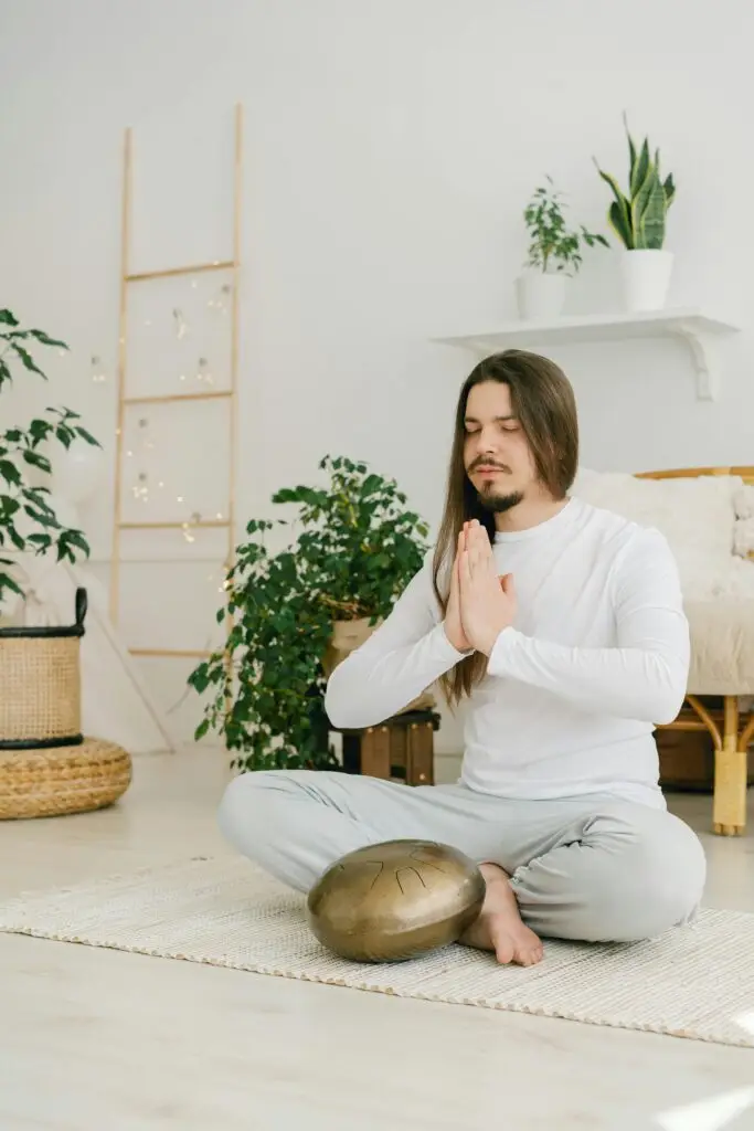A man practicing meditation indoors, sitting in lotus position with praying hands, fostering relaxation.