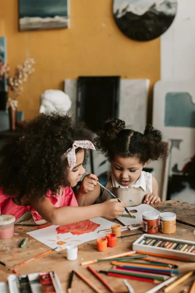Two young children joyfully painting together indoors, expressing creativity and art skills.